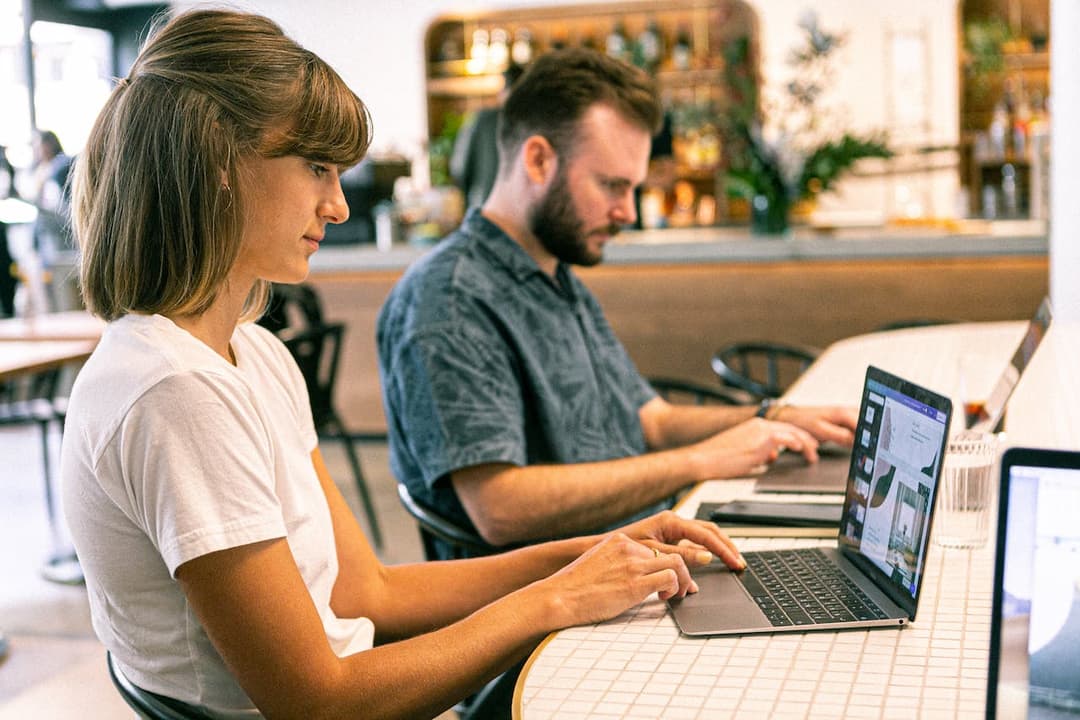 Two people working on laptops in a cafe setting